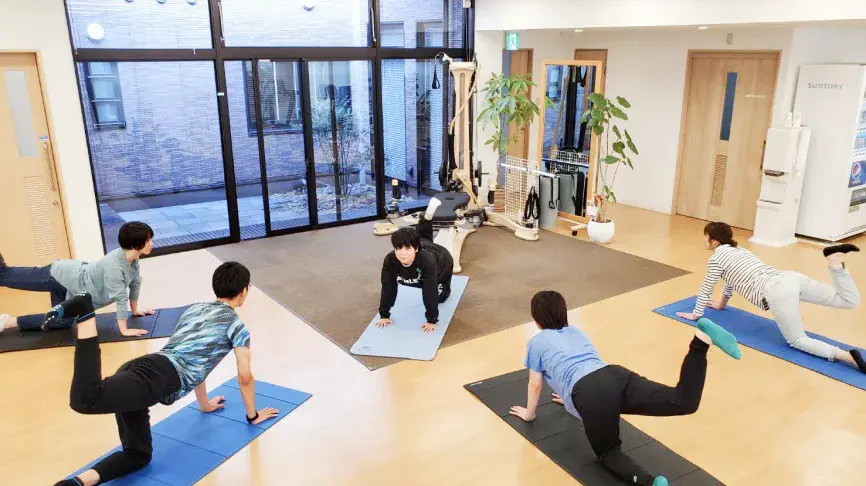 体幹を強化をマットを引いて運動する利用者と指導する理学療法士