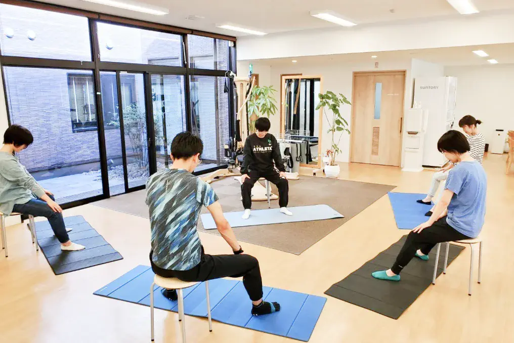 ジャイロキネシス®によるグループレッスンを受ける利用者と指導する理学療法士