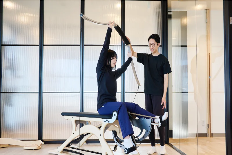 プログラムに沿って、O脚・X脚改善のレッスンする利用者とサポートする理学療法士