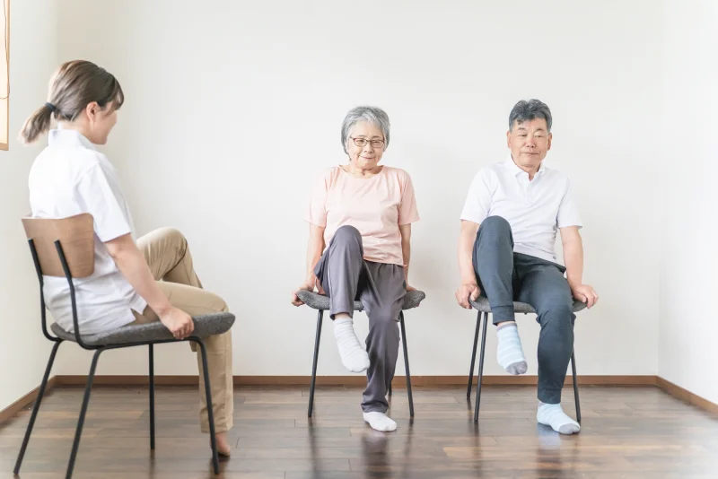 継続的な転倒予防サポートする理学療法士と椅子の上で運動する夫婦